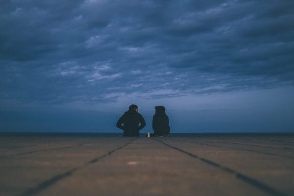 Two people sit on a jetty talking about addiction and mental health