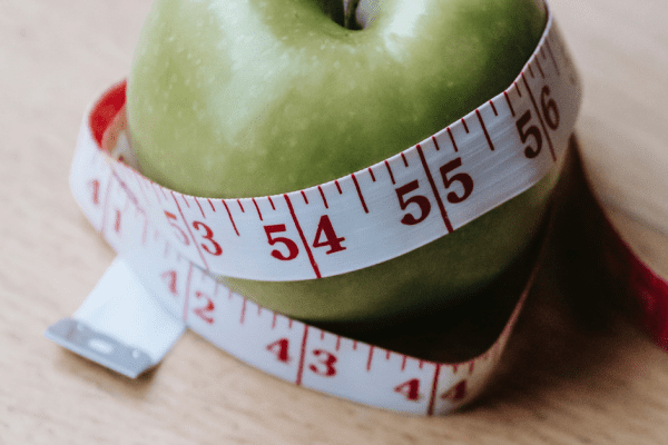 A green apple with a measuring tape around it