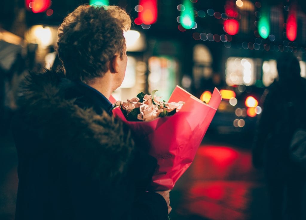 Man holds flowers as he anxiously waits for date.
