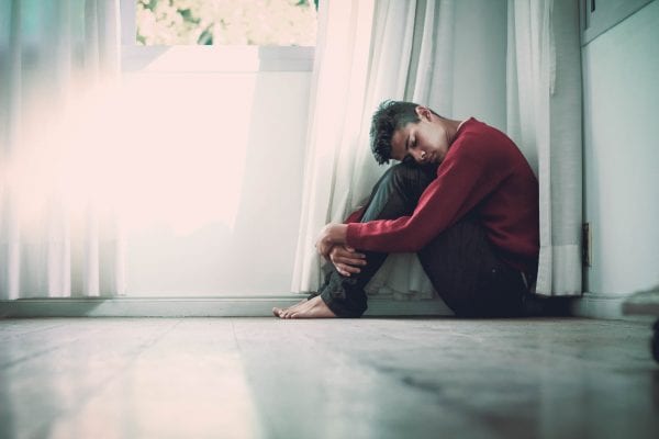 A man sitting on the floor, his face on his knees
