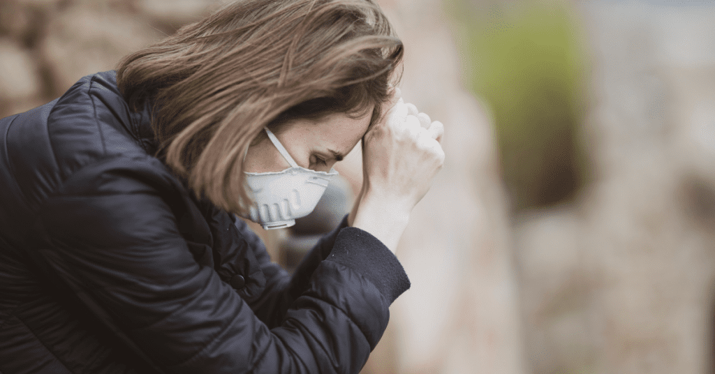 Woman wearing mask slumped over a handrail looking stressed.