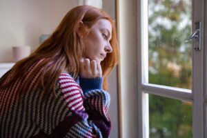 Seasonal depression is more than just the ‘winter blues’. A woman seated next to a rainy window with a wool jumper on to stay warm